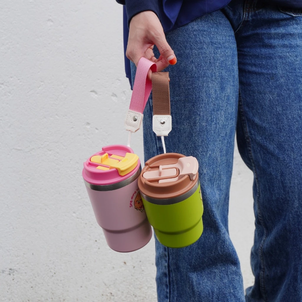 A person holding two Sipzz tumblers, one pink and one green.